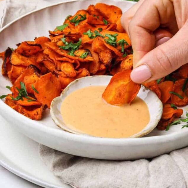 Golden crispy sweet potato chips served with creamy dipping sauce on a white plate, healthy snack option, vegan, gluten-free.