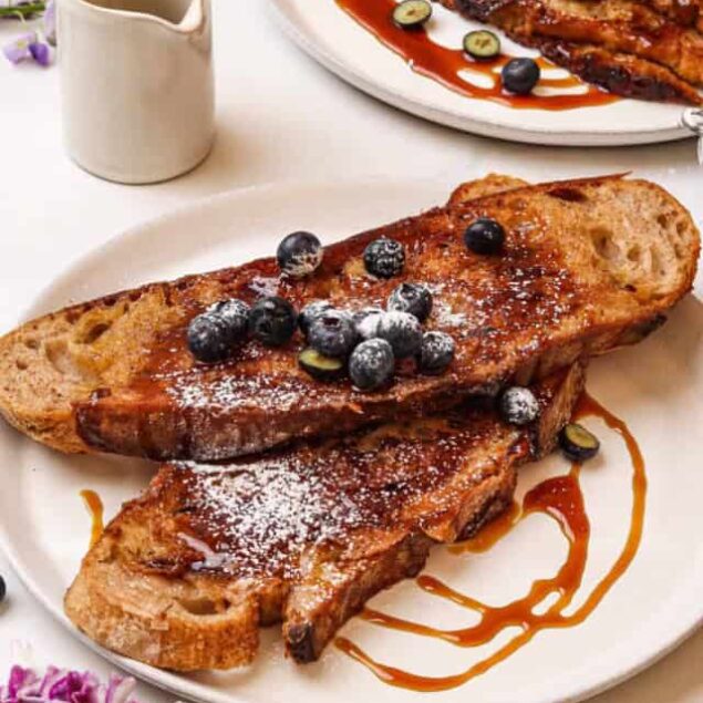Savory French toast with blueberries and caramelized syrup, served on a white plate, garnished with powdered sugar; perfect for brunch or breakfast delight.