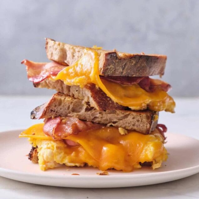 Juicy bacon and melted cheddar cheese breakfast sandwich on whole grain bread, served on a white plate. Perfect for a healthy start to your day with delicious, protein-rich breakfast options.