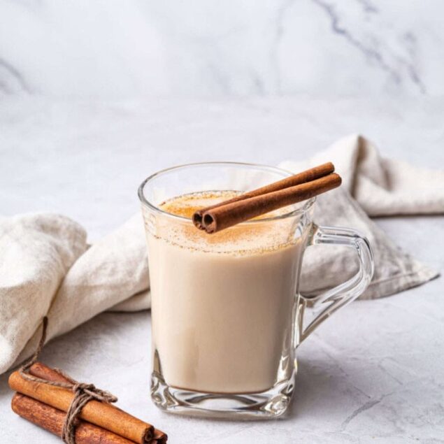 Creamy cinnamon spiced latte in a glass mug with cinnamon sticks on a marble surface for healthy coffee recipes and nutritious beverages.
