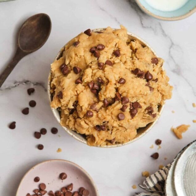 Rich chocolate chip cookie dough in a bowl with chocolate chips and baking ingredients on marble surface.