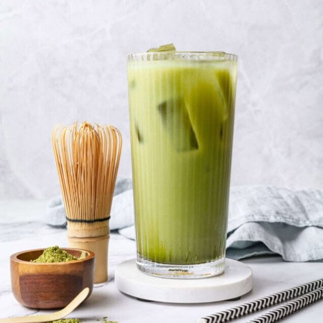 Matcha green tea latte with ice in a tall glass, served with matcha powder and bamboo whisk for a healthy, energizing drink. Perfect for wellness, weight loss, and anti-inflammatory benefits.