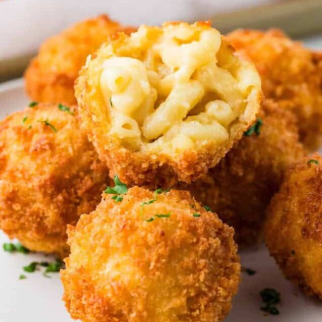 Golden crispy mac and cheese balls with creamy cheesy filling, perfect for appetizer or snack, on a white plate garnished with fresh herbs.