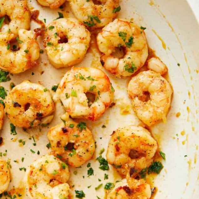 Juicy sautéed shrimp garnished with fresh herbs in creamy garlic sauce served in a white dish.