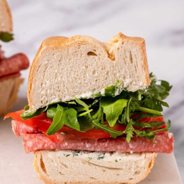 Fresh homemade hero sandwich with salami, leafy greens, and fresh bread on a light background.