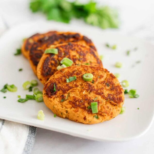 Grilled salmon patties with a crispy exterior and garnished with chopped green onions on a white plate. Healthy seafood recipe perfect for nutritious meals and meal prep.