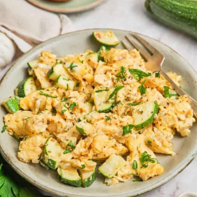 Scrambled eggs with zucchini and fresh herbs on a modern ceramic plate, healthy breakfast idea.