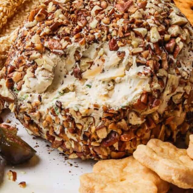 Roasted garlic herb cheese ball coated with chopped nuts on a serving platter with croissants and vegetables, perfect for healthy eating and entertaining.