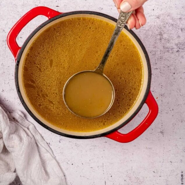 Warm homemade chicken broth in a red soup pot. Bone broth made with nutritious chicken bones, perfect for healthy eating and weight management. Ideal for meal prep and boosting immunity.
