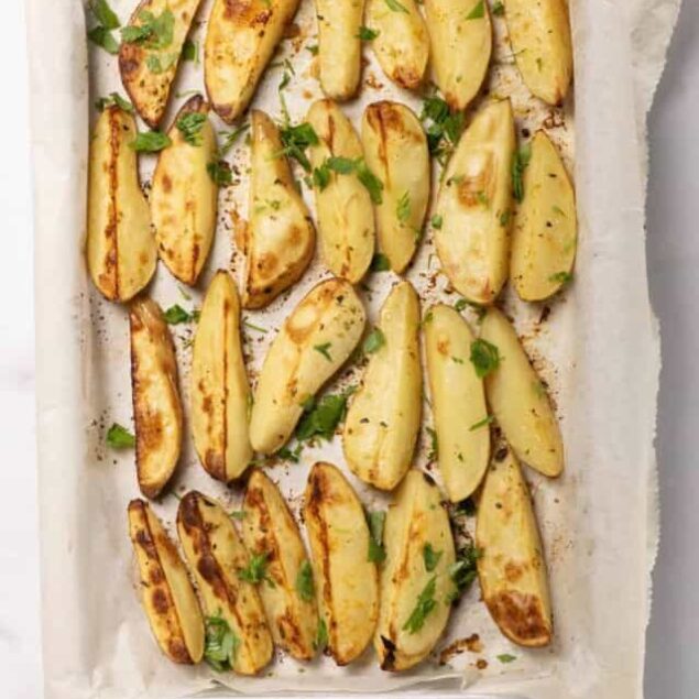 Golden roasted potato wedges garnished with fresh parsley on a parchment-lined baking sheet. Perfect healthy side dish for any meal or snack. Easy and delicious baked potato wedges recipe.