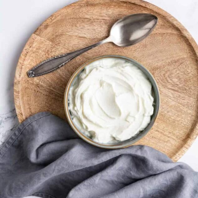 Creamy Greek yogurt in a bowl on a wooden tray, with a vintage spoon and gray cloth, highlighting healthy eating and nutritious food options for a balanced lifestyle.