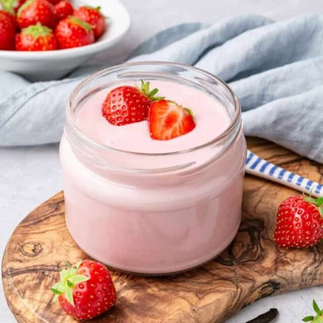 Creamy strawberry yogurt served in a jar with fresh strawberries on top and surrounding the wooden board, emphasizing healthy breakfast ideas and fruit-based snacks.