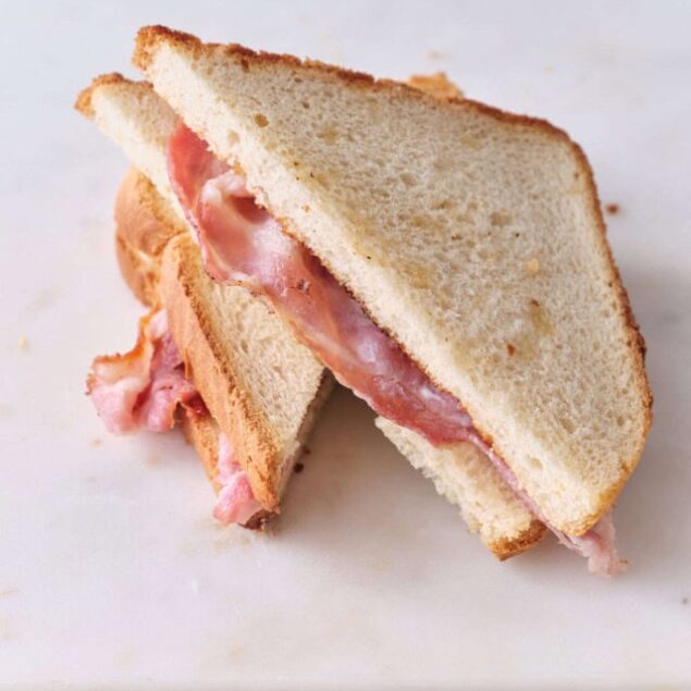 Golden toasted sandwich with ham and melted cheese on white marble surface.