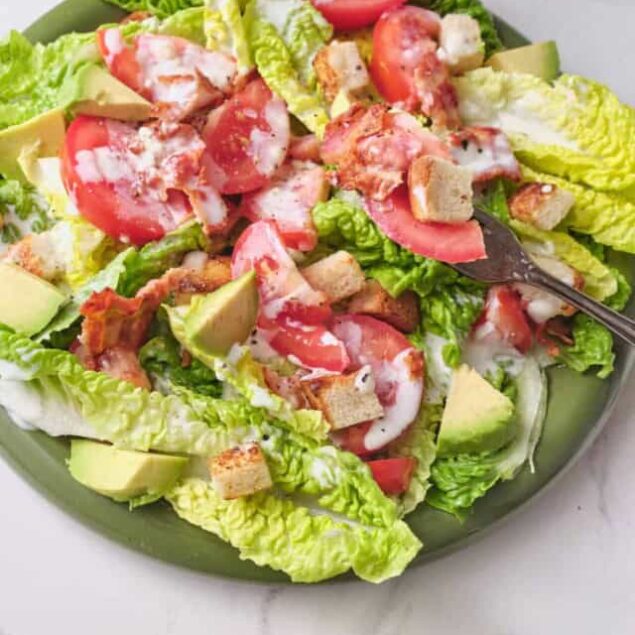 Fresh vegetable lettuce salad with tomatoes, avocado, croutons, and creamy dressing on a green plate. Perfect for healthy meals, weight loss, and clean eating.