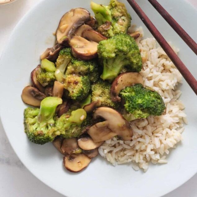 Steamed broccoli and mushroom stir-fry served with brown rice on a white plate, healthy vegetarian vegan meal, minimalistic white background.