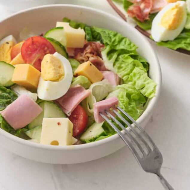 Fresh garden salad with boiled eggs, cheese, ham, cucumber, tomato, and leafy greens, served with a light dressing. Perfect healthy meal or side dish for balanced eating.