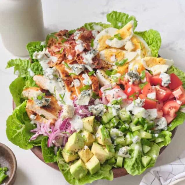 Fresh grilled chicken salad with boiled eggs, tomatoes, cucumbers, avocado, blue cheese, and red onions on a bed of lettuce, perfect for healthy eating and meal prep.