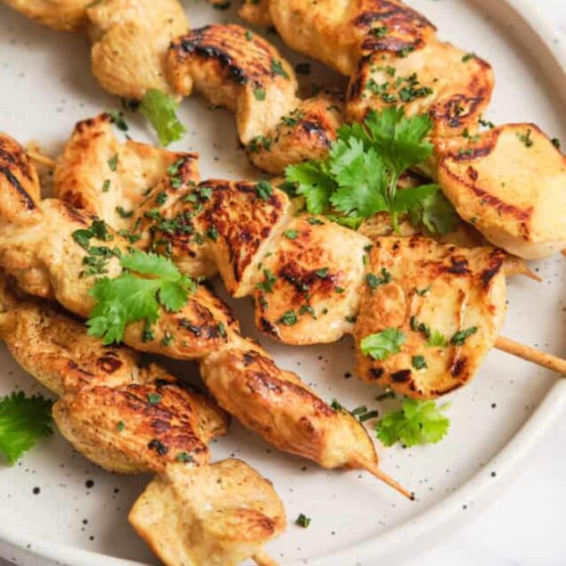 Grilled chicken satay skewers with fresh cilantro on a white plate, healthy protein-rich meal perfect for weight loss and nutritious eating.