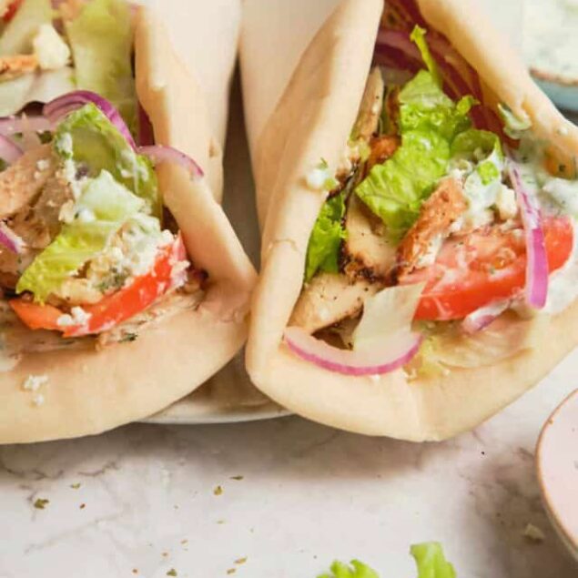 Fresh chicken pita sandwiches filled with lettuce, tomatoes, cucumbers, and red onions, served on a marble surface, showcasing healthy meal ideas from Food Faith Fitness.