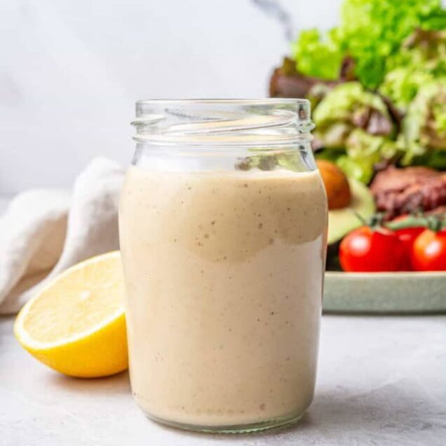 Creamy homemade salad dressing in a glass jar with fresh vegetables and leafy greens in the background, emphasizing healthy eating and nutritious recipes.