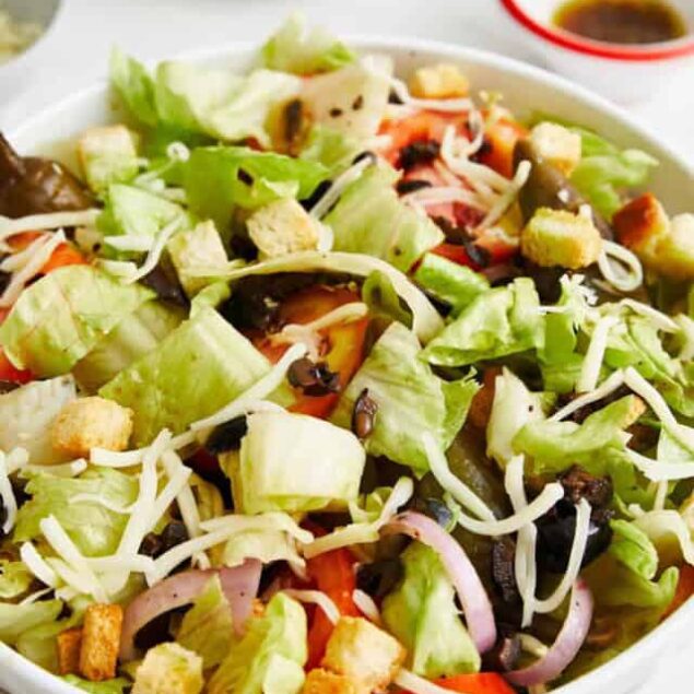Fresh homemade healthy taco salad with lettuce, tomatoes, cheese, onions, croutons, and black beans served with a side of dressing. Perfect for nutritious, high-protein meals.
