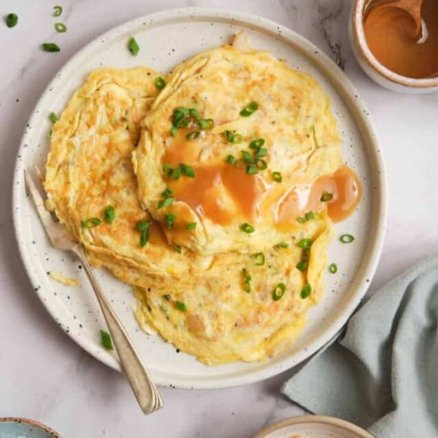 Creamy scrambled eggs withOC smooth texture, topped with green onions and drizzled with caramelized honey sauce, served on a white plate for a nutritious breakfast.