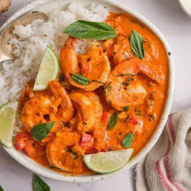Succulent shrimp in a creamy, spicy tomato sauce served with fluffy white rice and fresh lime wedges, garnished with basil leaves for a flavorful seafood dish.