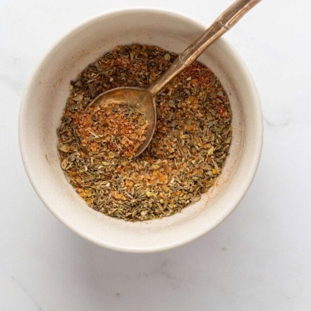 Dried herb and spice blend in a white bowl with a spoon, ideal for healthy cooking and flavoring meals.