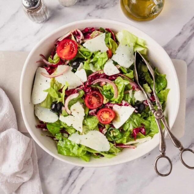 Fresh garden salad with cherry tomatoes, mixed greens, shaved parmesan, olive oil and balsamic vinegar on a white marble surface healthy and nutritious meal for weight loss and wellness.