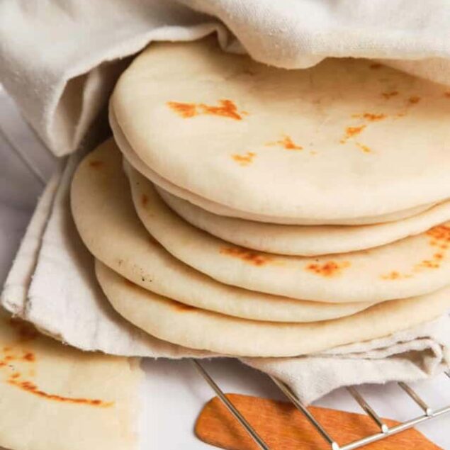 Soft, freshly made flour tortillas stacked on a cloth with a tortilla board and knife, perfect for healthy meal prep and homemade Mexican recipes.
