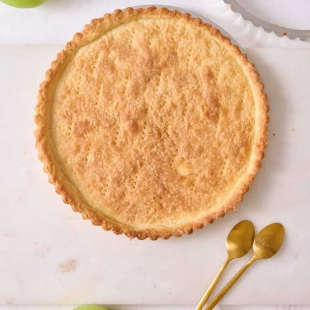 Buttermilk pie with a golden crust on white background, fresh green apple and gold dessert spoons, homemade healthy dessert, simple dessert recipe, easy pie recipe.