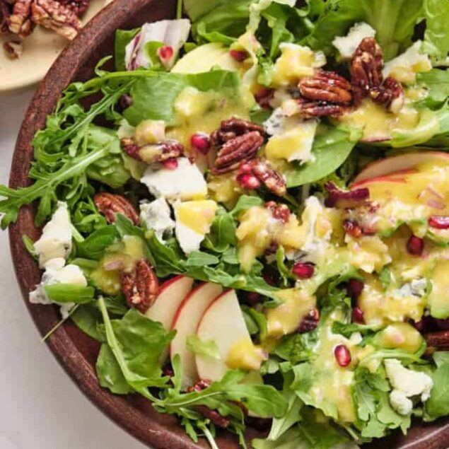 Fresh green salad with mixed greens, sliced apples, blue cheese crumbles, pecans, pomegranate seeds, and a tangy vinaigrette dressing for a healthy and delicious meal.