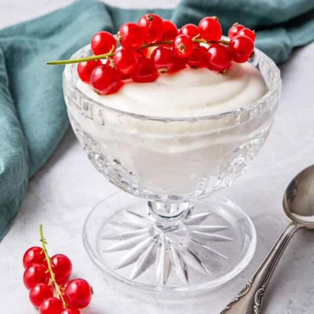 Red currants on a glass dessert cup filled with creamy yogurt or panna cotta, topped with fresh red berries, served on white marble surface with vintage spoon and teal napkin - healthy dessert recipes, fresh fruit toppings.