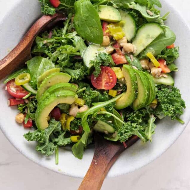 Fresh veggie salad with cucumbers, cherry tomatoes, avocado, kale, and chickpeas in a white bowl, perfect for healthy eating and weight loss.