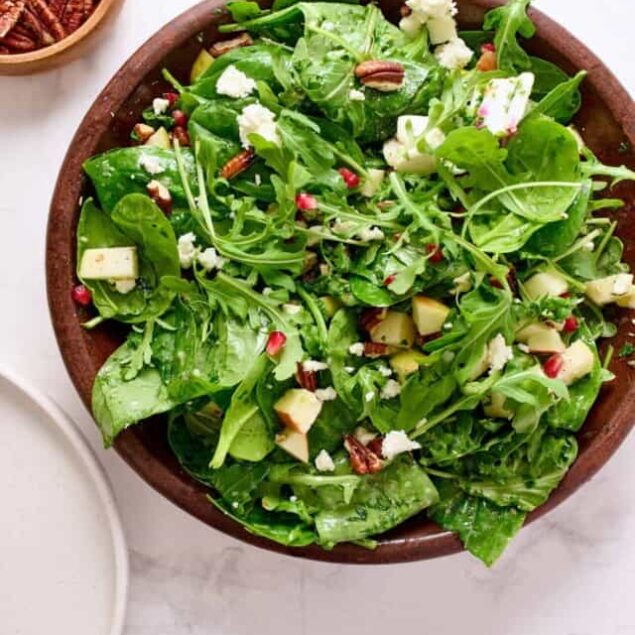 Fresh spinach and arugula salad with walnuts, cheese, and pomegranate seeds in a wooden bowl, healthy and nutritious vegetarian meal option from Food Faith Fitness.