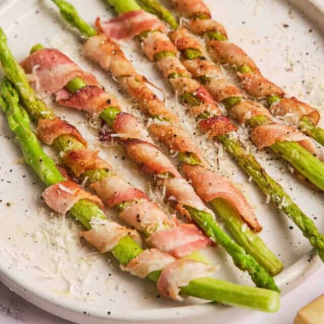 Roasted asparagus wrapped in prosciutto on a white plate, garnished with grated Parmesan cheese, healthy appetizer or side dish, perfect for nutritious meals.