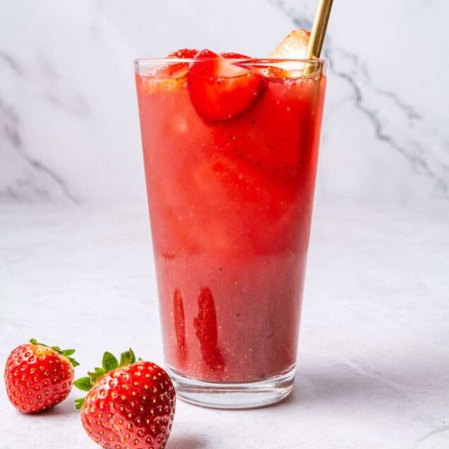 Fresh strawberry smoothie with ice served in a tall glass with a gold straw, on a white marble background. Perfect for healthy eating and fitness detox drinks.
