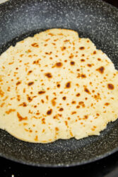 Gluten-free flatbread cooking in a speckled pan, lightly browned.