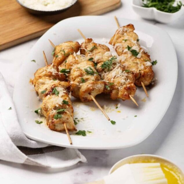 Grilled chicken skewers garnished with herbs on a white plate, served with rice, fresh herbs, and lemon. Healthy and delicious meal from Food Faith Fitness.