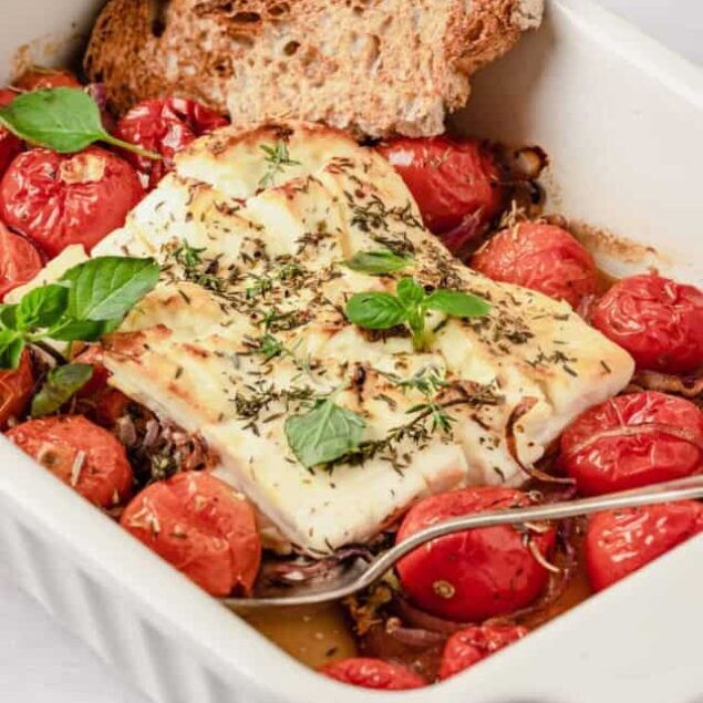Savory baked cod with cherry tomatoes and fresh herbs in a white baking dish, served with toasted whole grain bread, healthy and delicious dinner recipe, Food Faith Fitness.