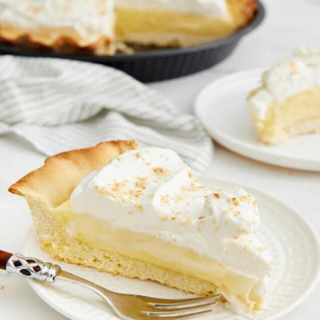 Creamy lemon meringue pie slice on white plate, topped with fluffy meringue and toasted with a golden brown finish, perfect for dessert or sweet treats.