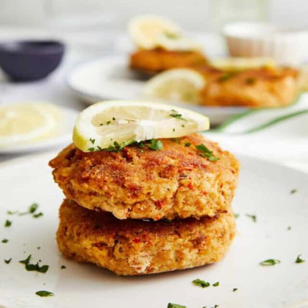 Crispy baked fish cakes garnished with lemon slices and fresh herbs on a white plate, healthy seafood recipe, ideal for balanced eating and meal prep.