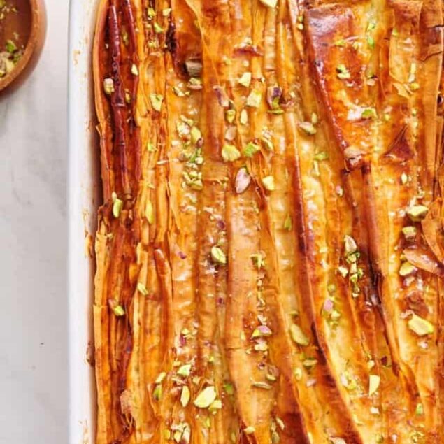 Golden baked caramelized banana foster dessert with chopped pistachios in a white baking dish.