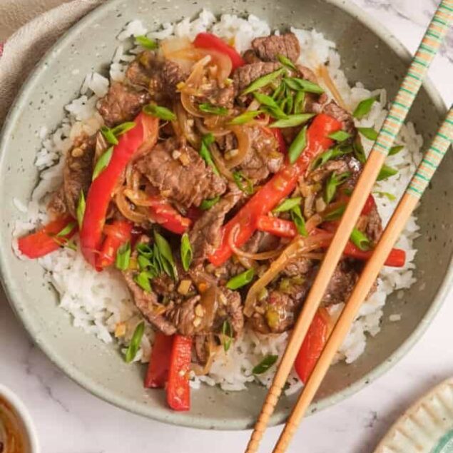 Juicy beef stir-fry with red peppers, onions, and green onions served over fluffy white rice, healthy and delicious Asian-inspired meal.