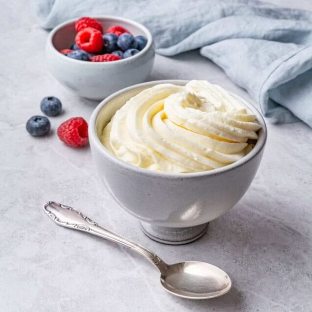 Creamy vanilla yogurt with a swirl of whipped topping in a white bowl, served alongside fresh berries on a light gray surface. Perfect for healthy breakfast or snack ideas from Food Faith Fitness.