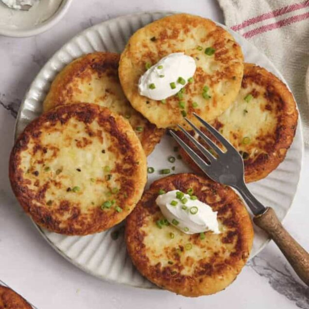 Golden crispy potato pancakes topped with sour cream and chopped green onions on a white plate. Perfect for healthy comfort food recipes and gluten-free meal options.