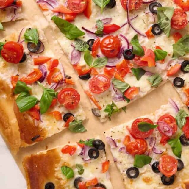 Fresh veggie pizza with cherry tomatoes, black olives, red onions, and basil toppings on a crispy crust - a healthy and delicious meal option.