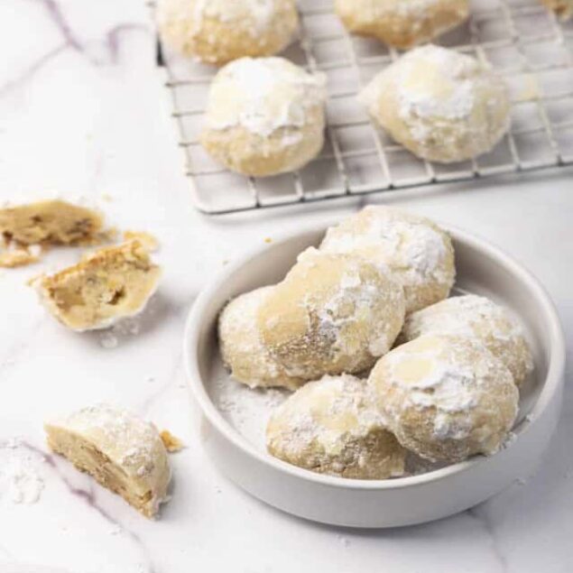 Chewy lemon snowball cookies with powdered sugar on a white marble surface and in a small white bowl, perfect for healthy dessert recipes.