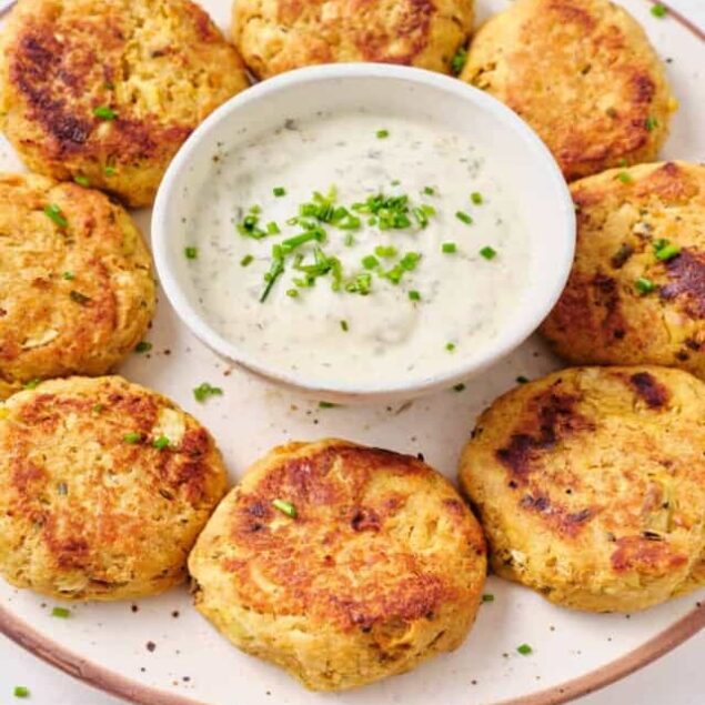 Golden baked crab cakes with a creamy dill dipping sauce on a white plate.