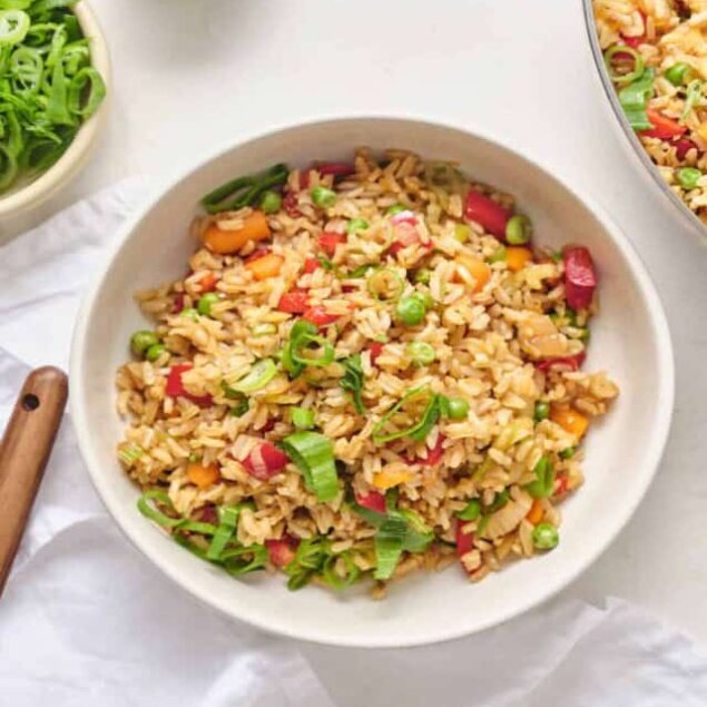 Savory veggie fried rice with peas, carrots, and green onions in a white bowl for healthy meal recipes.